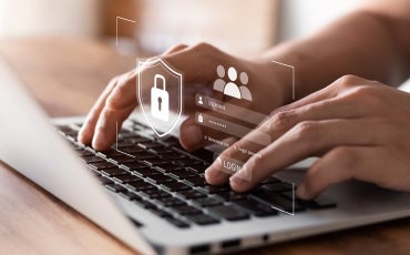 Close-up of hands typing on a laptop keyboard with digital graphics showing a padlock, user icons, and login fields, symbolizing online security and user authentication.