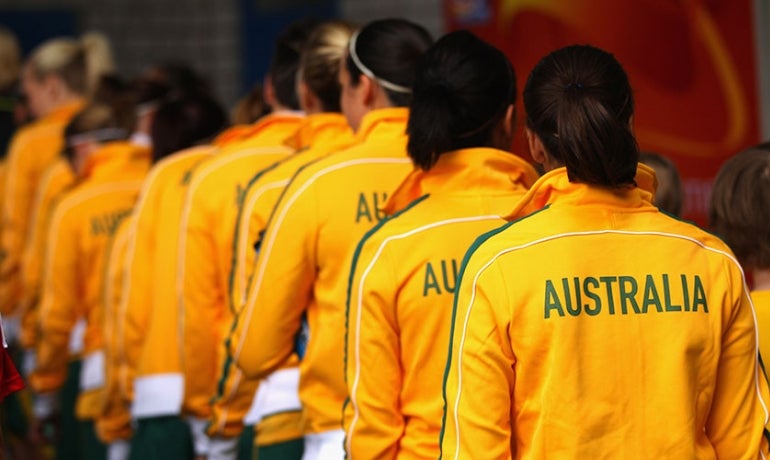 A line of athletes wearing yellow jackets with AUSTRALIA printed on the back, standing close together with their backs to the camera.