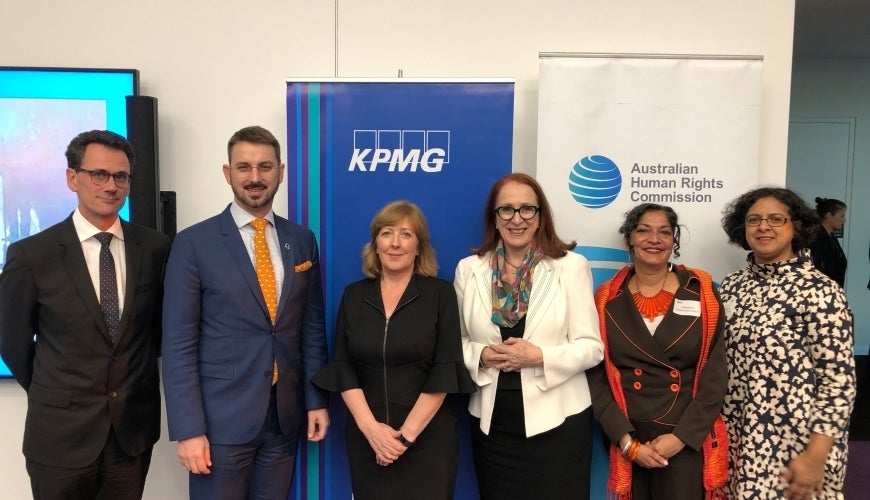 Six professionally dressed people stand in a row, smiling, in front of KPMG and Australian Human Rights Commission banners at an indoor event.
