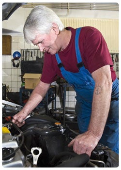 An elderly man working on the car engine