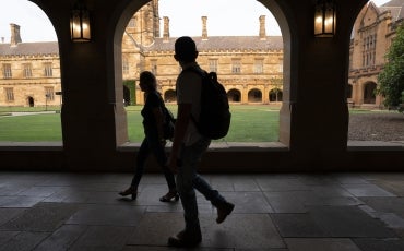 Image of shadowed university students walking through open corridor alongside university quadrangle