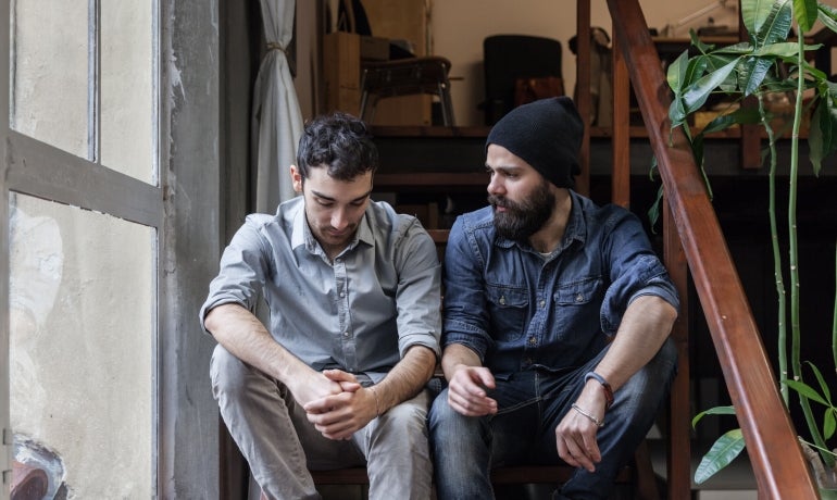 Two young men dressed casually sitting on wooden stairs in an office having a discussion