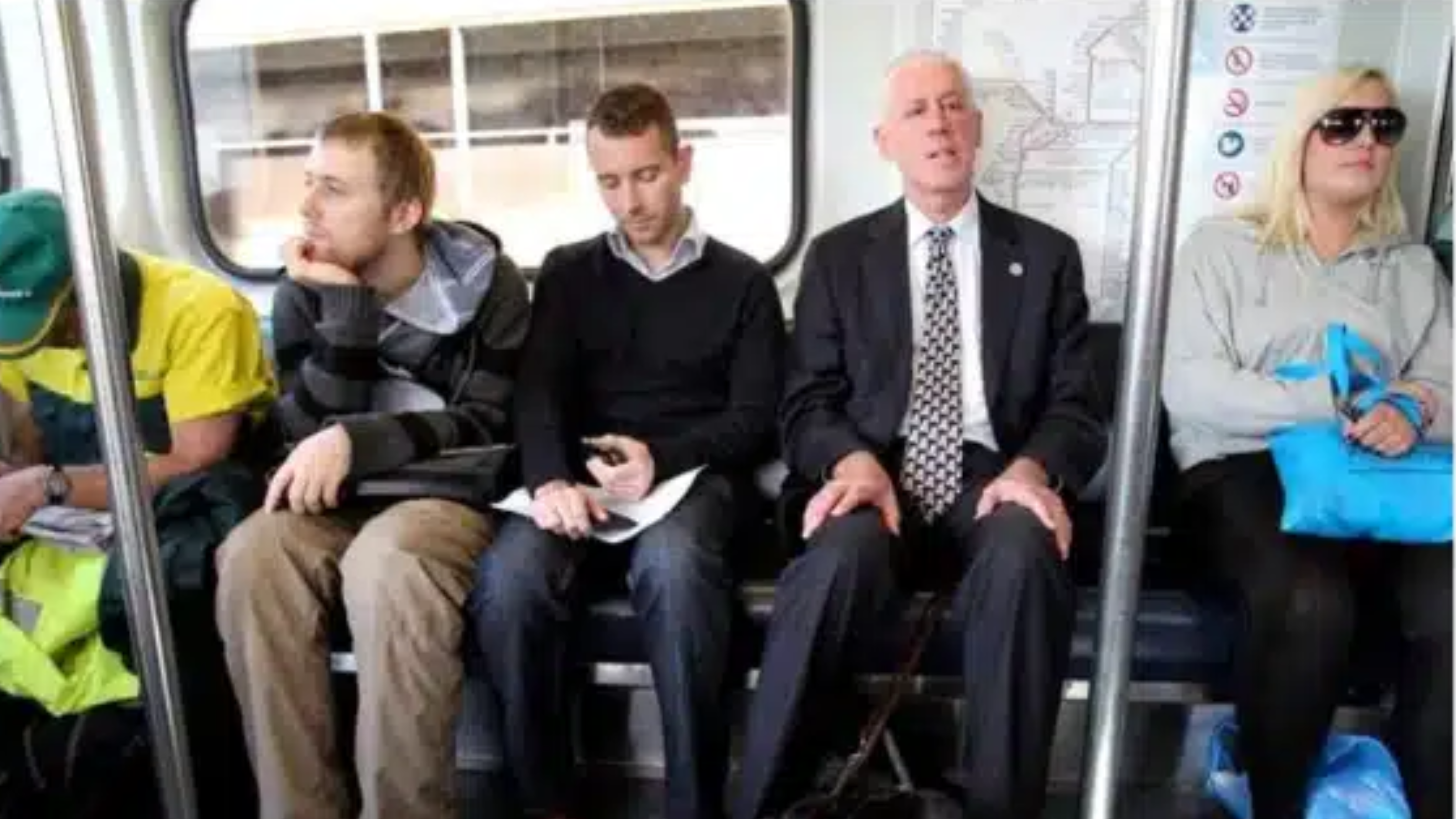 Four men are sitting inside a train carriage. The man second from the right is Graeme Innes.