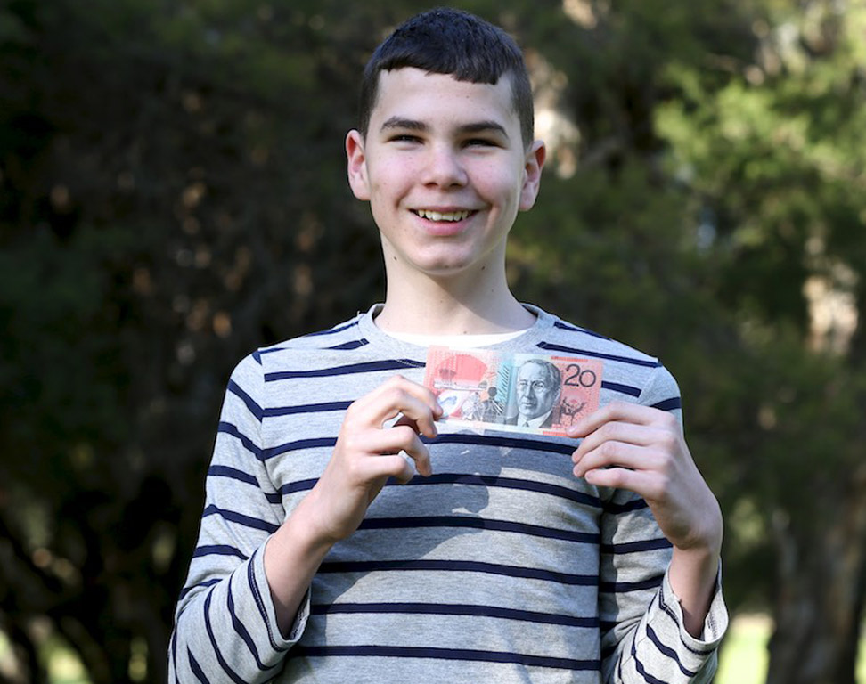 A young teenage boy in a blue and white striped shirt is holding up a 20 dollar note