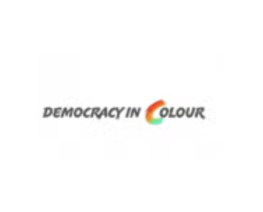 The image shows the text DEMOCRACY IN COLOUR with the letter C in COLOUR depicted as a colourful, gradient arc in red, orange, yellow, and green. The rest of the text is in black on a white background.