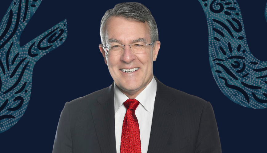 A man with short hair and glasses wearing a dark suit, white shirt and red tie