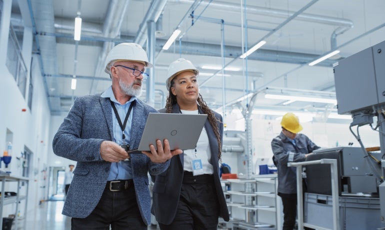 One older white male engineer with grey beard and middle age black engineer wearing hard hats in an industrial setting