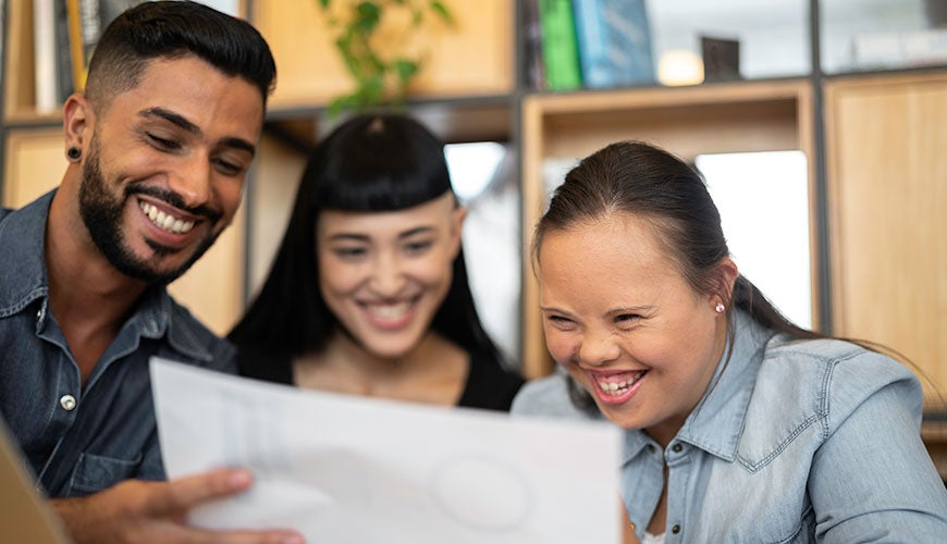 Three people smiling and looking at a workplan together, one of whom has Down Syndrome