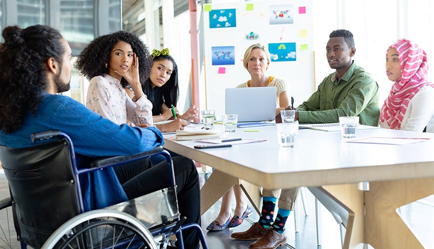 People sitting at a boardroom table, one of who is in a wheelchair