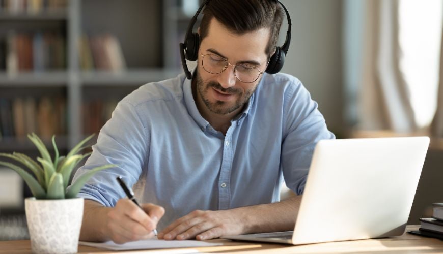 A man with headphones on sitting at a desk studying