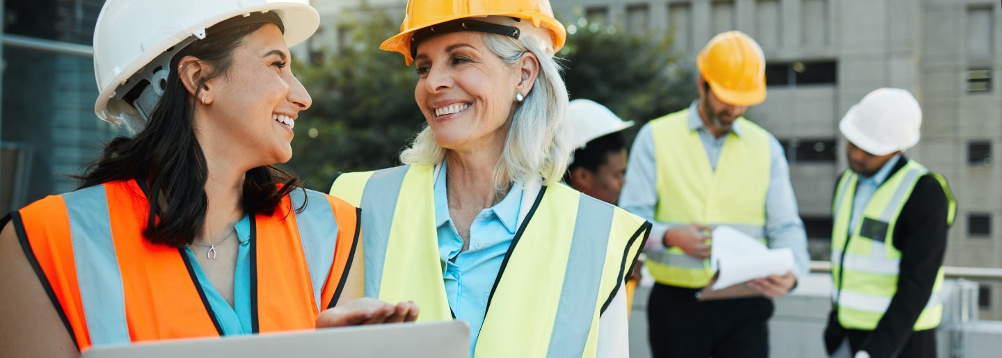 Two ladies in construction hats smile at each other