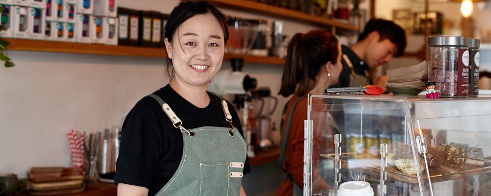 Shop owner smiling whilst working inside coffee shop.