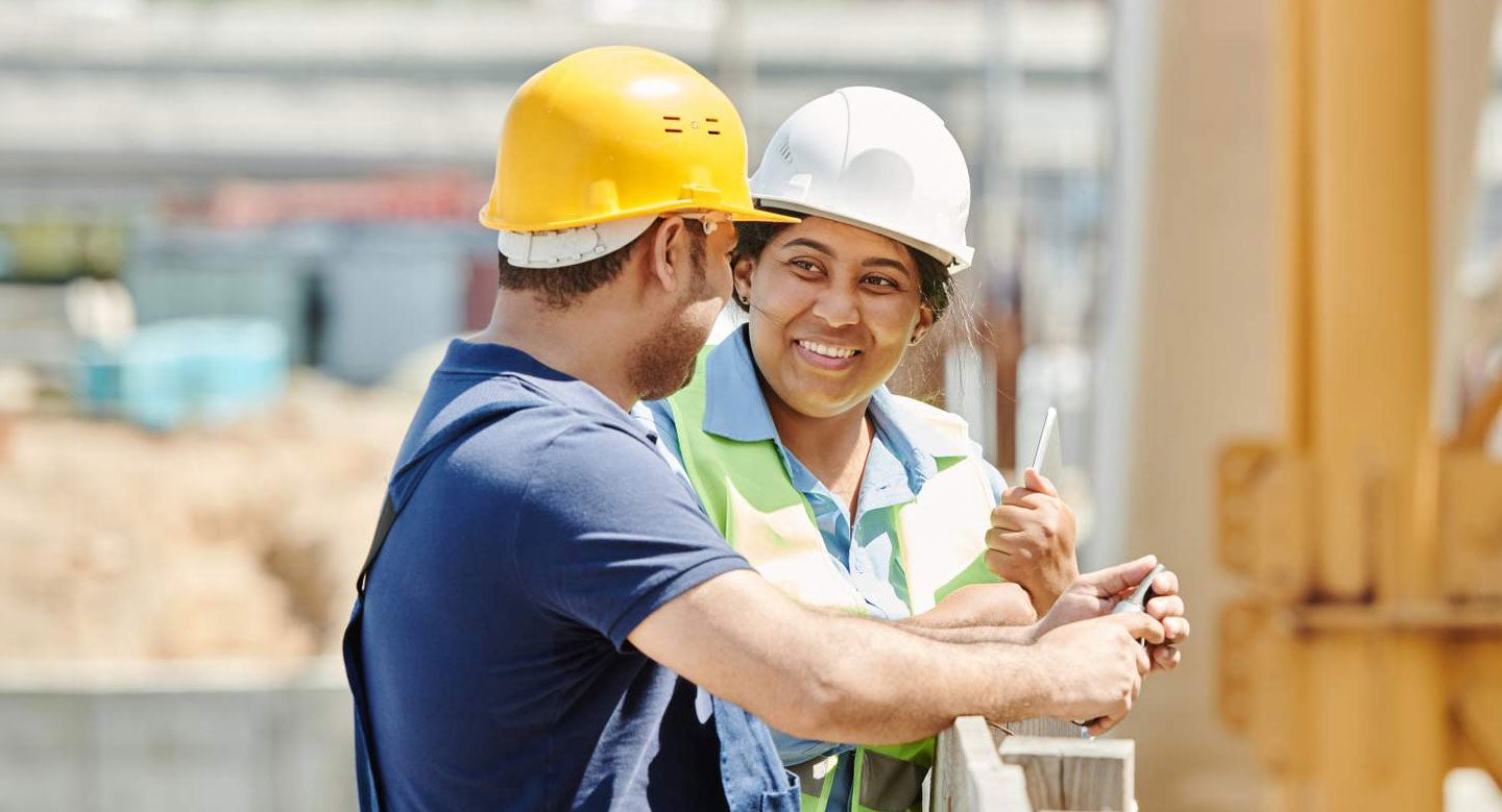 A smiling woman and a man work on a construction site.