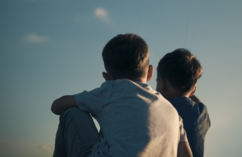 Two children sitting down looking at blue sky