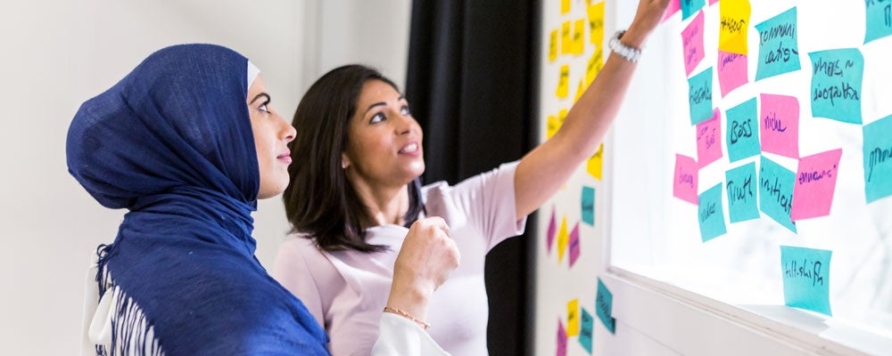 Two diverse ethnic women discuss ideas with sticky posted notes.