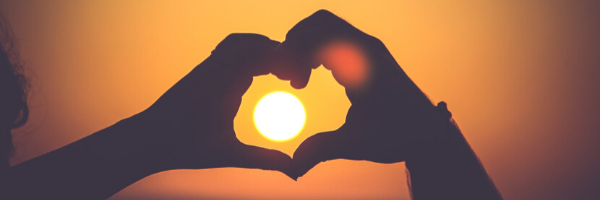 Hands making heart across sunset