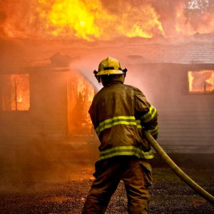 A fireman hosing a large fire out of a house