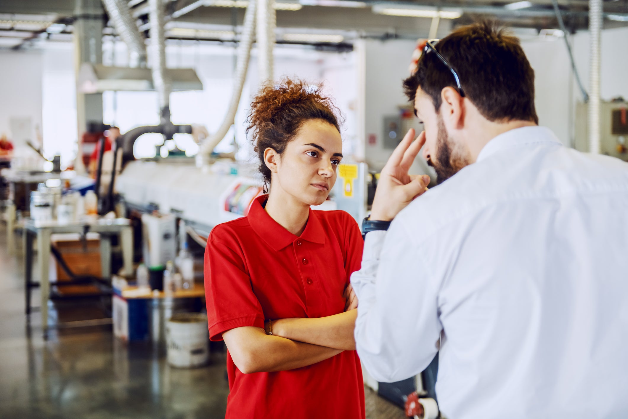 Young female print shop worker listening with arms crossed to male supervisor yelling