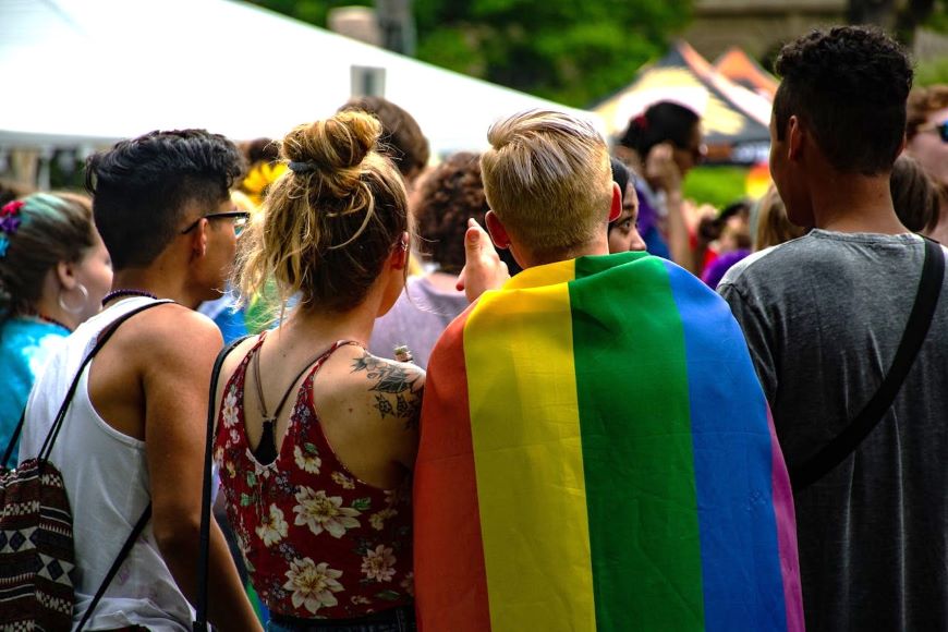 A group of young people at an LGBTQIA+ event. One person has the rainbow flag around their shoulders.
