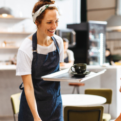 Cafe worker smiles while serving customer seated at table