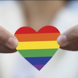 Fingers holding onto a cut out rainbow coloured heart 