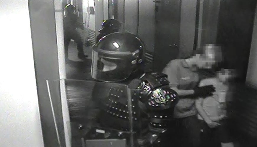 still from incident video: guard in body armour on alert and another guard leads child away
