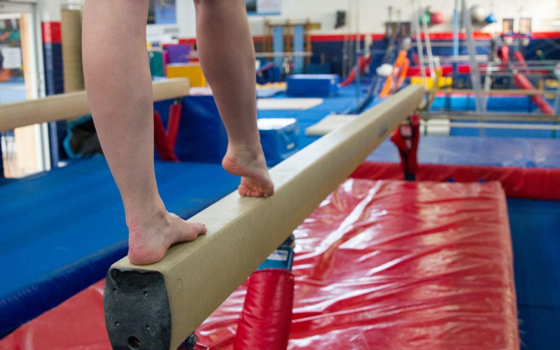 The legs of a child gymnast seen standing on a balance beam.