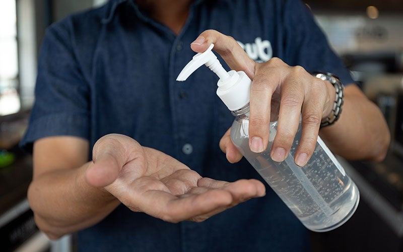 A person holds a bottle of hand sanitiser and pumps it into their hand.