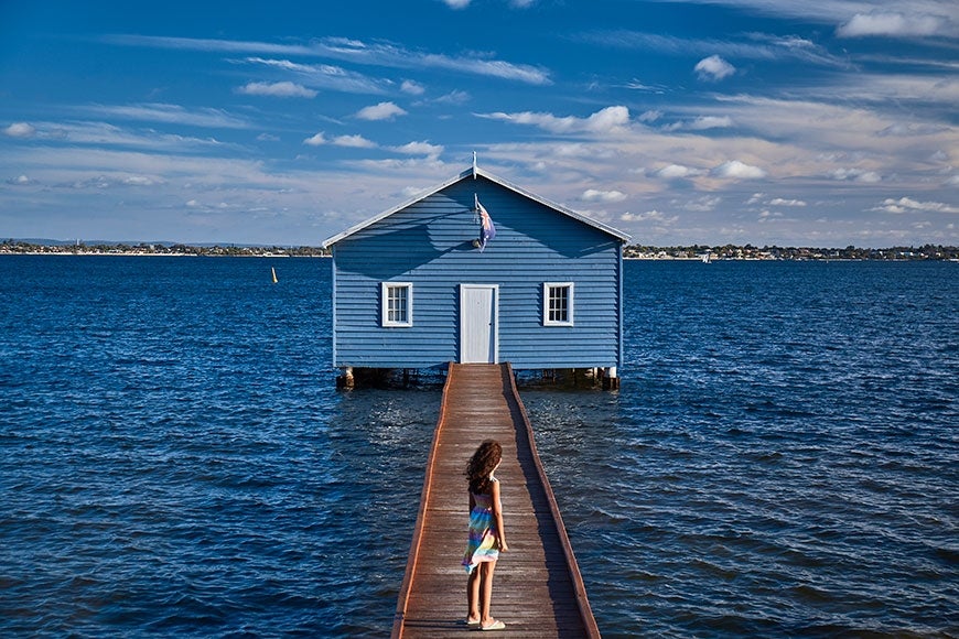 A girl standing on bridge surrounded by water and a house in front
