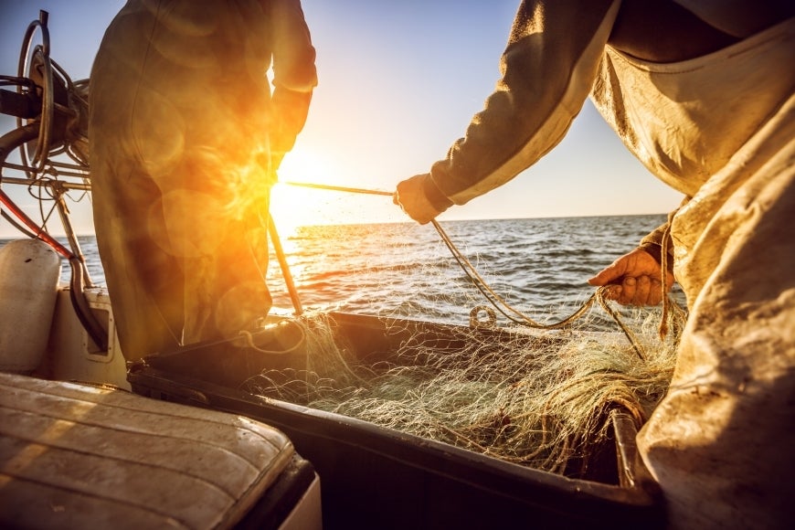 Two fishermen on a boat pulling nets