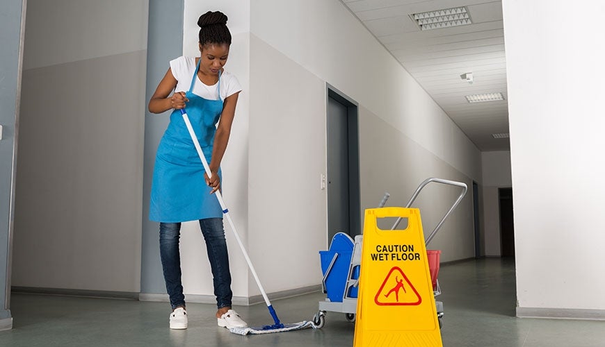Cleaner in office building with a 'caution wet floor' sign