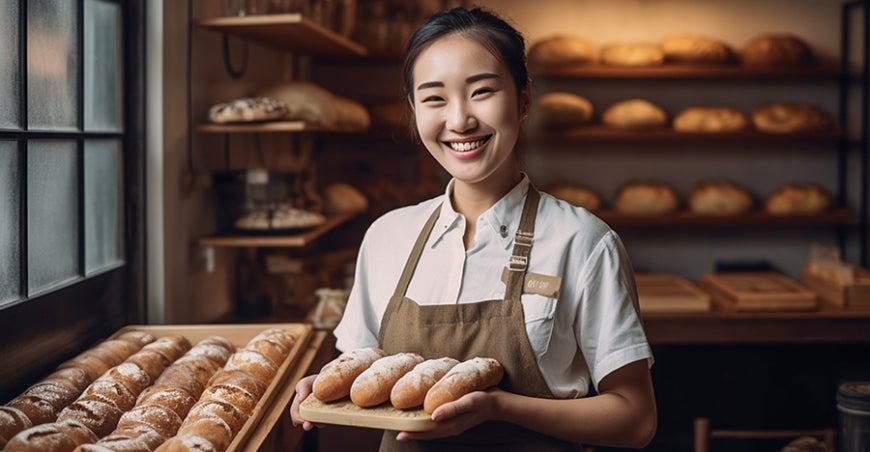 Smiling woman in a bakery holding bread rolls