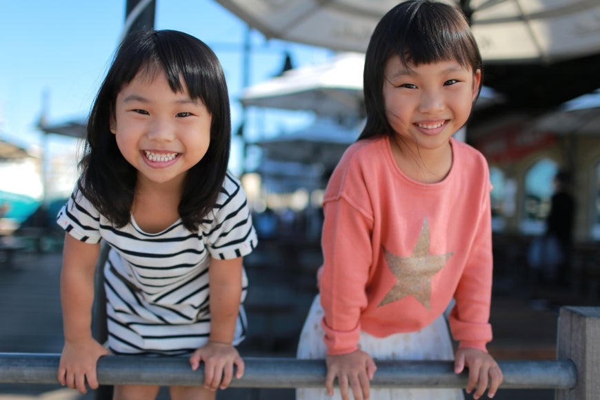 Two Asian girls smiling happily playing outdoors.