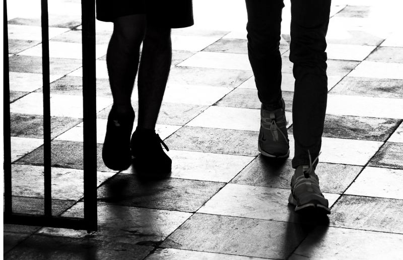 Black and white image showing the legs of a schoolboy and girl as they walk on chequered tiles.