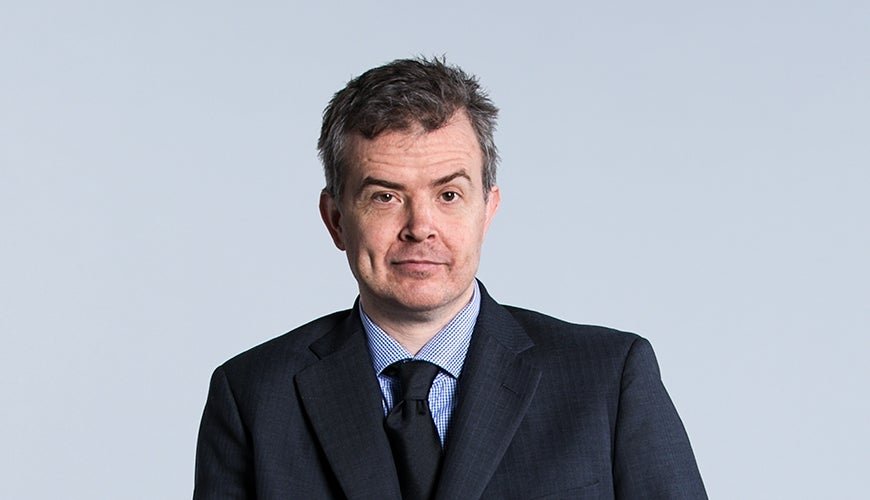 Portrait of Ben Gauntlett, who uses a wheelchair. He is wearing a suit and looking to the camera.