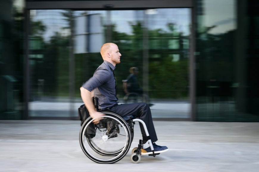 A young man using a wheelchair moves through a city street.
