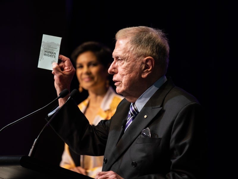 Man at lectern holding up piece of paper
