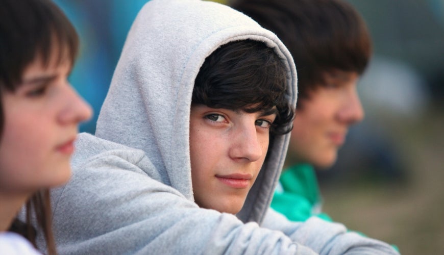 Focus teenage boy in grey hoody gazing thoughtfully sitting between two peers