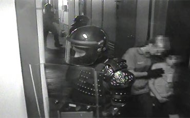 still from incident video: guard in body armour on alert and another guard leads child away