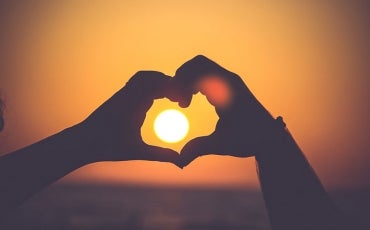 Hands framing a heart over a sunset