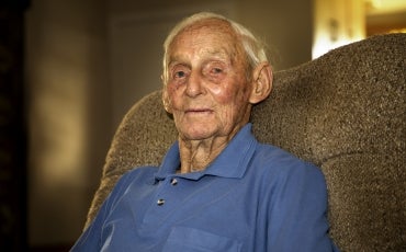 An elderly man sitting on a sofa at home, looking into the camera.