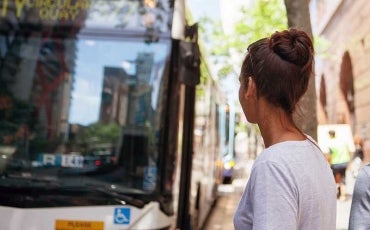 A young woman waits for a bus on a city street.
