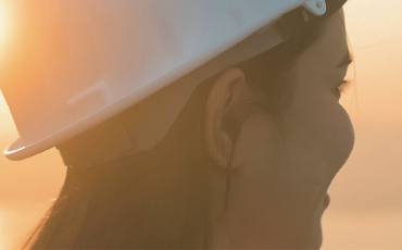 A woman wearing a white hard hat smiles into the distance