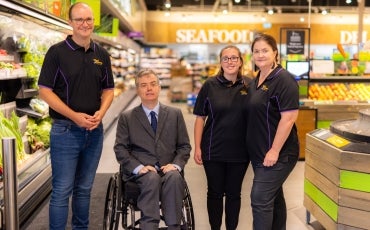 Dr Ben Gauntlett sits in a wheelchair in a Woolworths store with three Good Sammy staff standing around him.