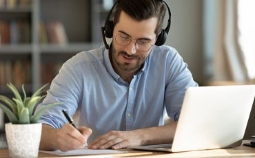 A man with headphones on sitting at a desk studying