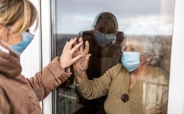 two women wearing surgical masks touching hands with a window between them