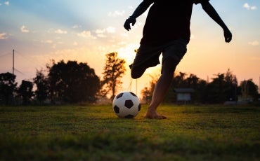 A young person plays soccer on an open field alone, with the sun setting behind them.
