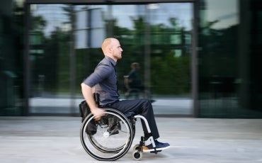 A young man using a wheelchair moves through a city street.