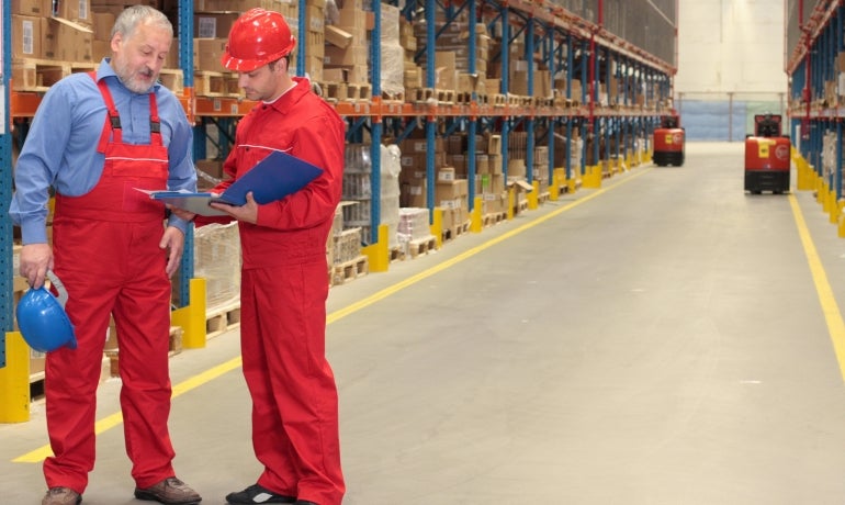 Older white male warehouse worker in discussion with his younger male collegue.