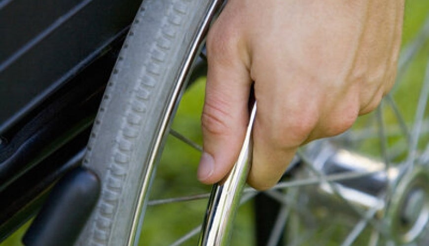 A close-up view of one wheel of wheelchair. A person is holding the wheel. 